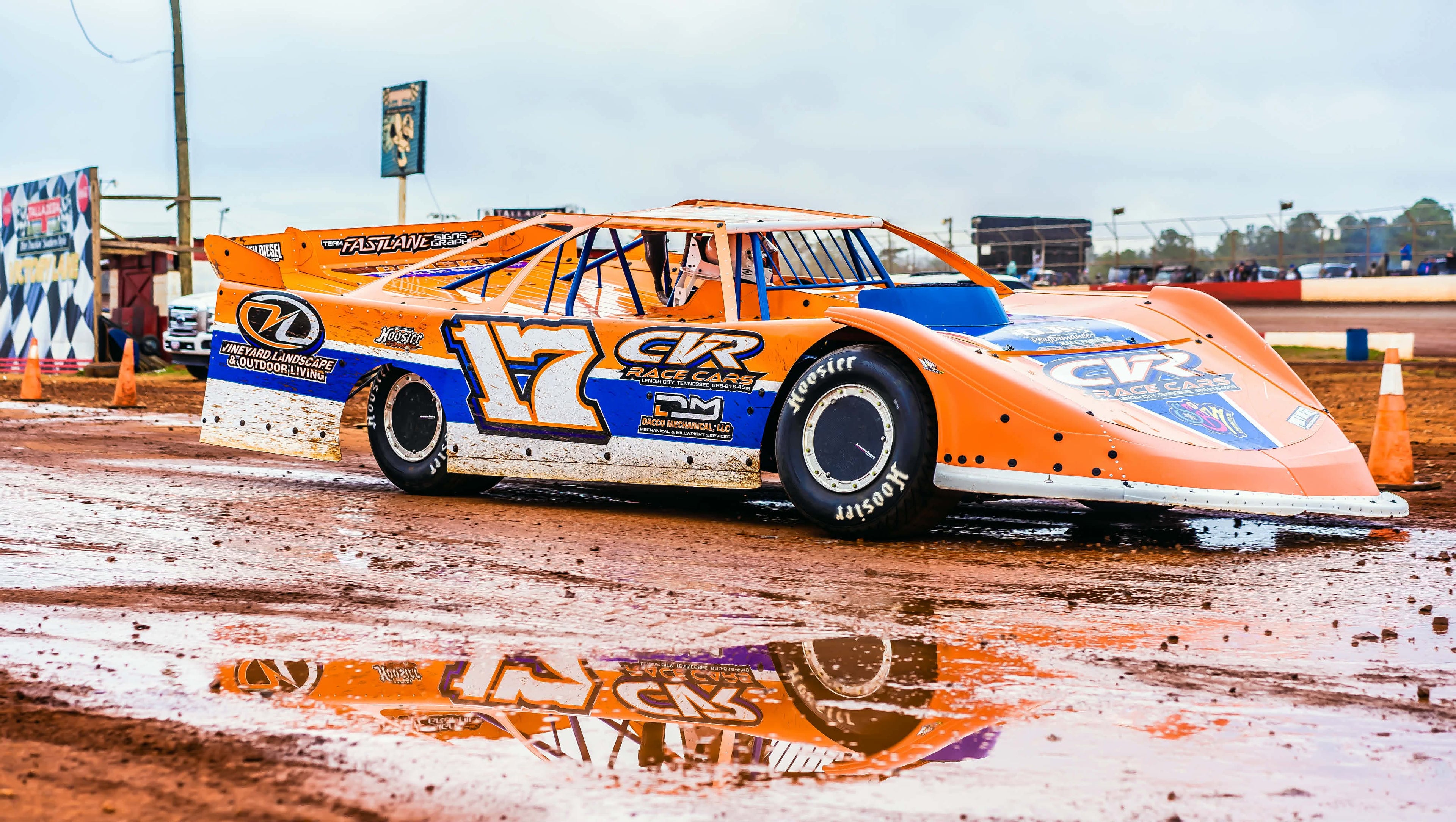 Orange and blue race car on a dirt track with visible branding.